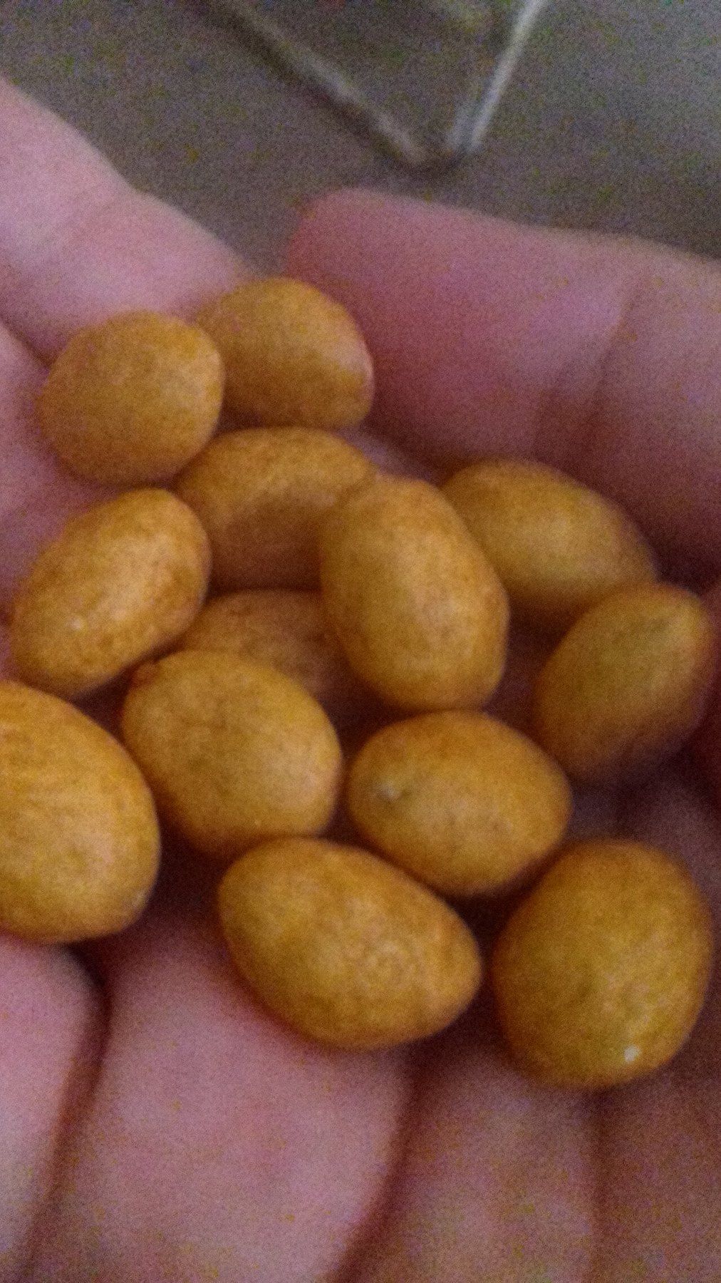 Un puñado de cacahuates japoneses en la palma de una mano: maníes cubiertos de una capa crujiente de color dorado.