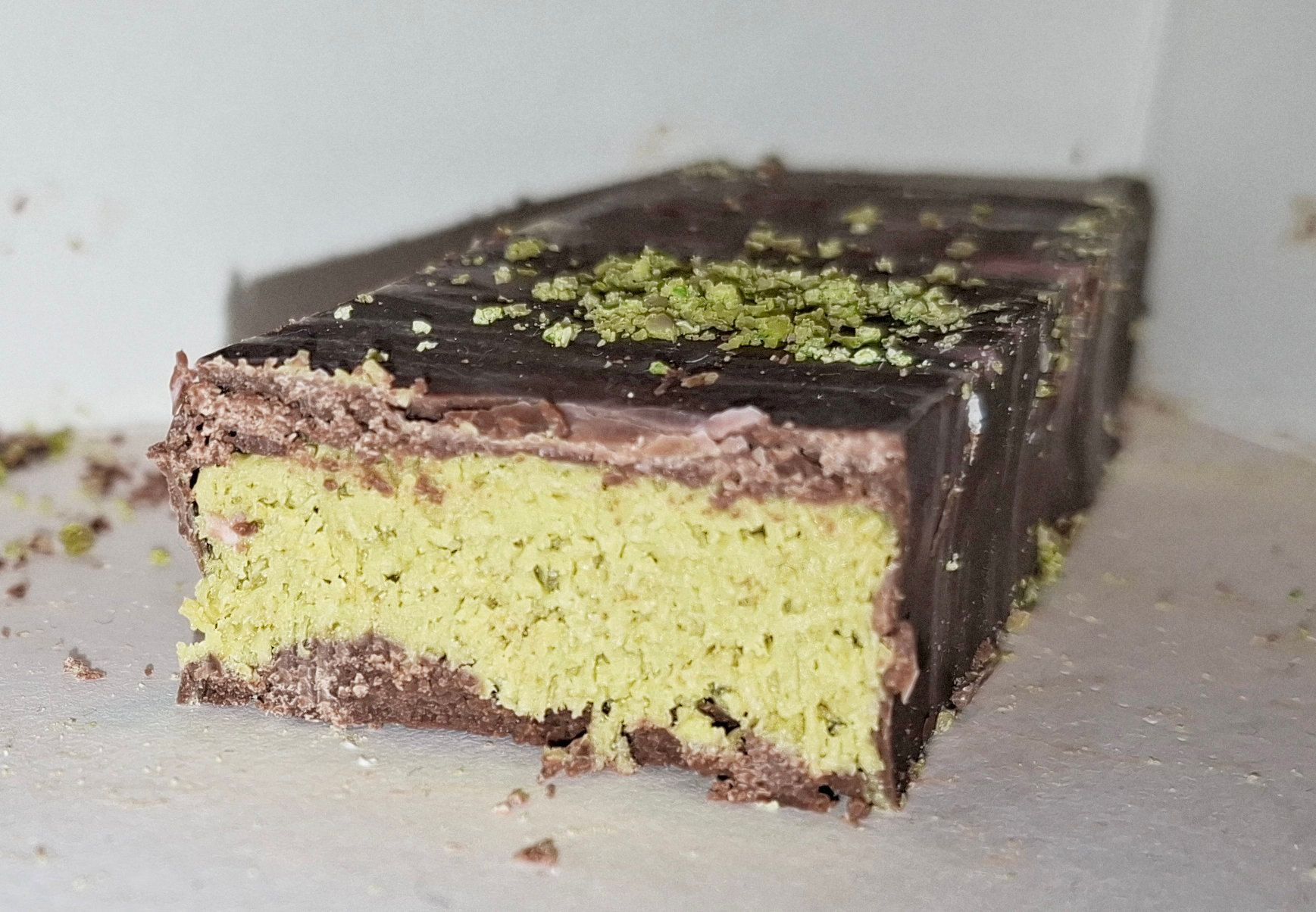 Una barra de chocolate cortada al medio que muestra un relleno verde de crema de pistacho con hebras crujientes.