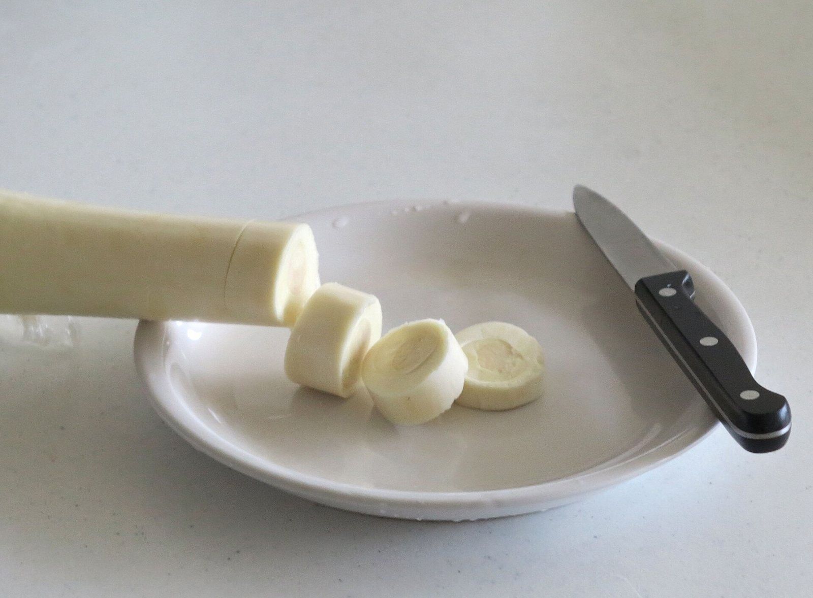 Un palmito fresco, largo y blanco, cortado en rodajas sobre un plato, con un cuchillo al lado.